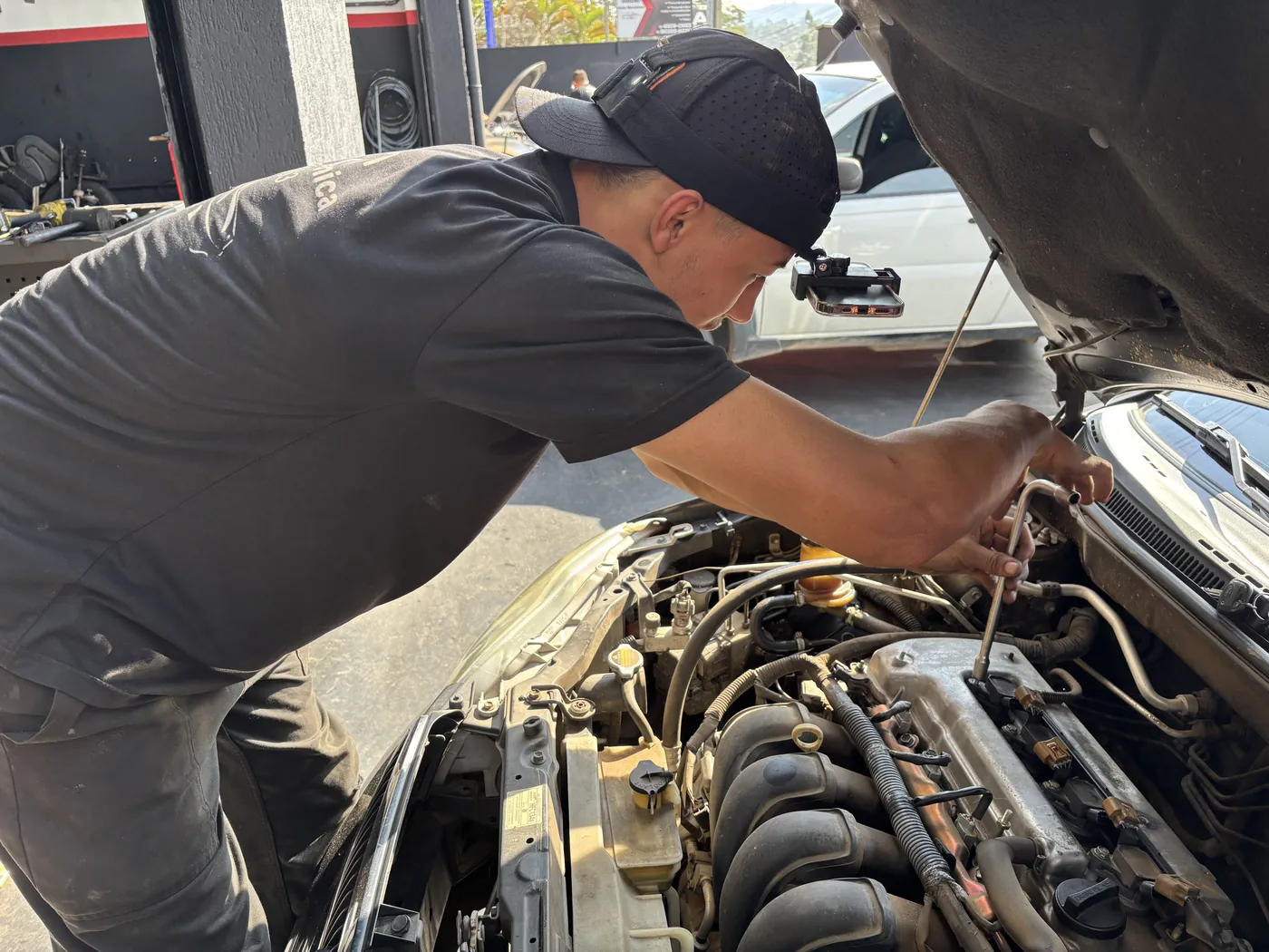 A mechanic working under a car bonnet, wearing a head rig
