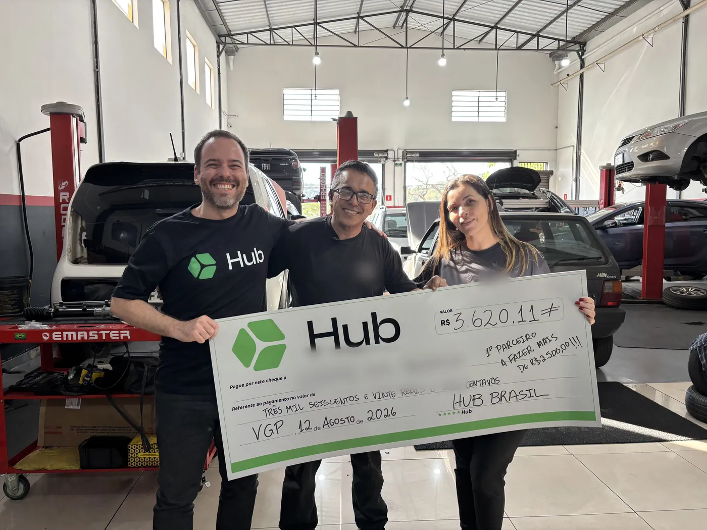A Hub teammate and an auto workshop team holding a giant Hub cheque